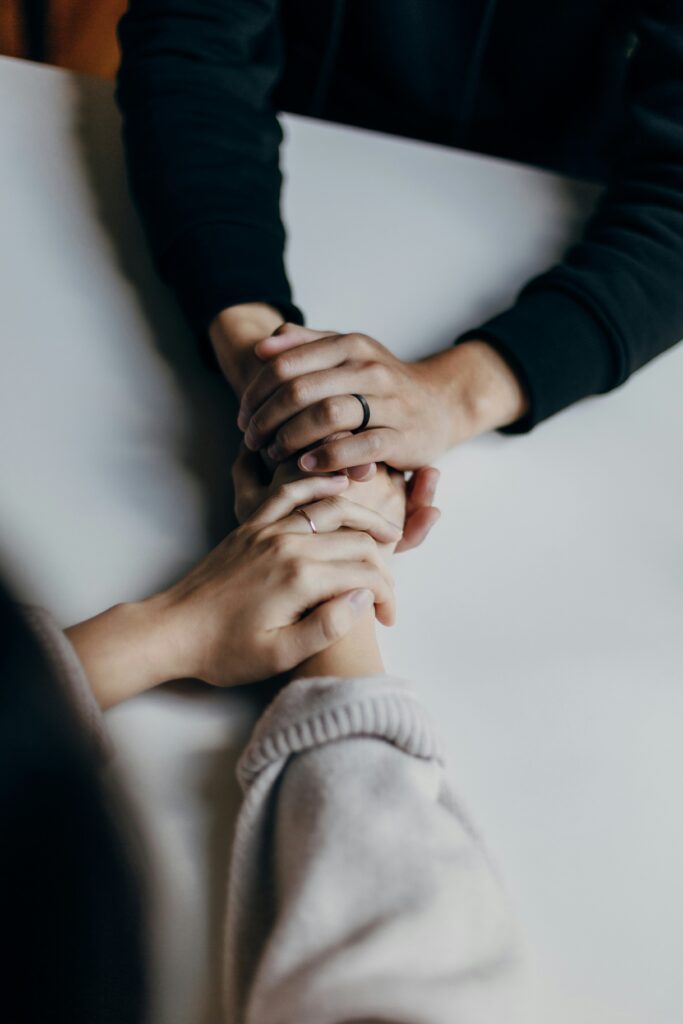 Two people holding hands across a table in a moment of comfort and support